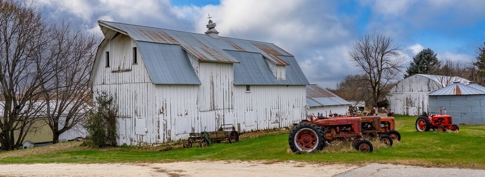 A white barn on a local farm with display of vintage tractors an a manuer spreader near Rochester MN
