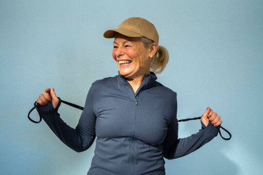 Happy senior woman looking away holding resistance band against colored background