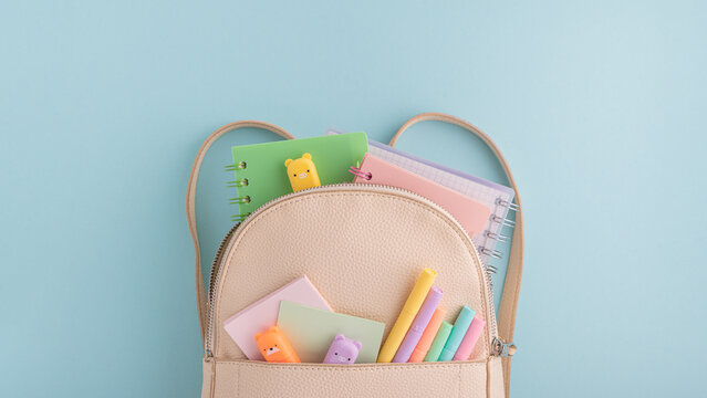 Pastel school supplies into backpack on blue background