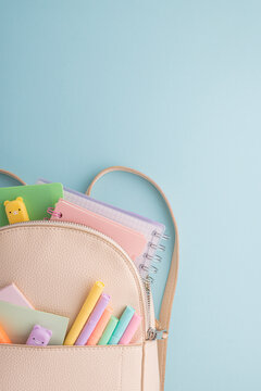 Pastel school supplies into backpack on blue background