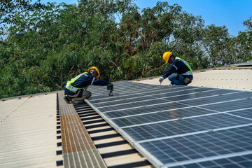 Fototapeta premium A professional technician in safety gear standing on a rooftop, preparing electrical wiring for a solar panel installation under a clear blue sky.