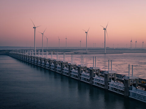 Aerial view of the Oosterscheldekering storm surge barrier and a row of wind turbines during a calm sunset.