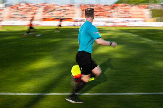 Blurred panning shot of a soccer linesman running along the sideline with a flag during a professional football match.