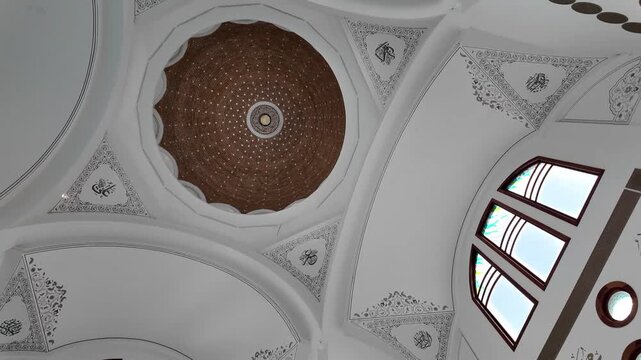 The main focus lies on the ceiling which has a brown inner dome with intricate geometric patterns, surrounded by artistic Arabic calligraphy at each corner of the arch.