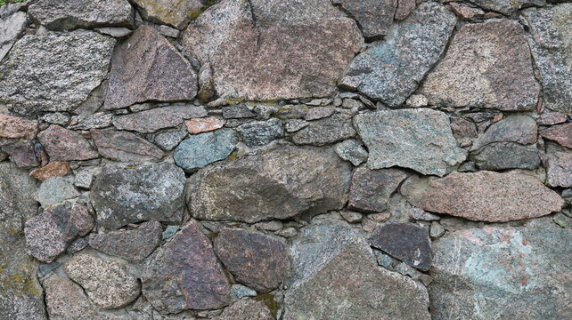 Beautiful rough stonework made of solid granite boulders and small pebbles, a fragment of a wall or fence made of natural rock, the texture of the stone material in the structure of the exterior