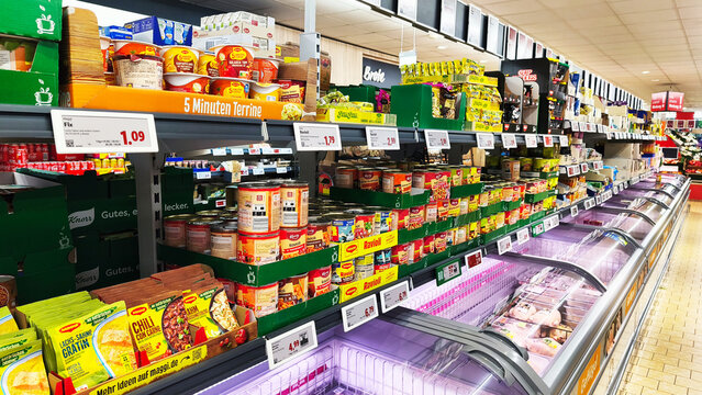 Iserlohn, Germany &mdash; May 06 2026: interior of a Lidl supermarket showing grocery aisles with Maggi 5 Minuten Terrine, canned food, and frozen meat section with price tags.
