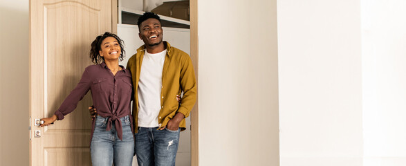 A couple stands at the doorway of their new home. They are smiling and embracing each other. The setting shows a bright, welcoming space behind them. © Prostock-studio