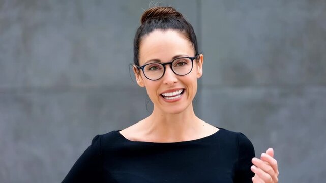 Static close up shot of woman smiling and speaking while gesturing against concrete wall background