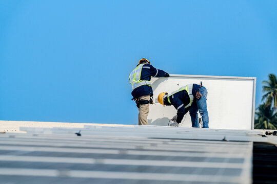 Two solar technicians working together to align and bolt down photovoltaic modules on a commercial roof during a sunny day.
