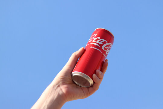 Kyiv, Ukraine - May 6, 2026: Hand holding a can of Coca-Cola against a blue sky background. Female hand holding a red aluminum can of classic Coca-Cola. Concept of refreshment and popular drinks