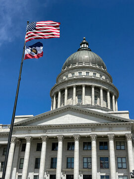 Utah State Capitol Building with American flag and Utah State flag against blue sky 