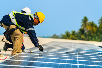 A professional technician in safety gear standing on a rooftop, preparing electrical wiring for a solar panel installation under a clear blue sky. © ultramansk