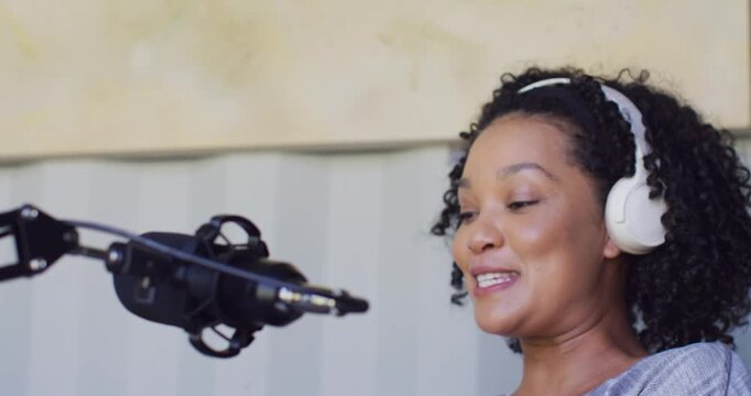 African American woman sitting in studio with headset starting recording for song, singing into mic