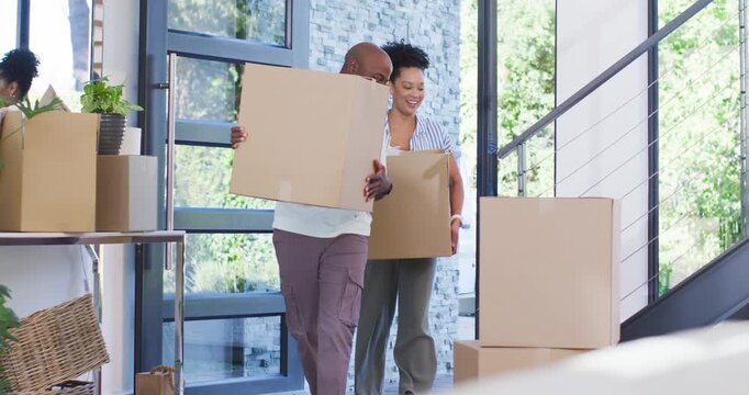 African American couple opening glass door, carrying boxes into foyer, moving in and stacking