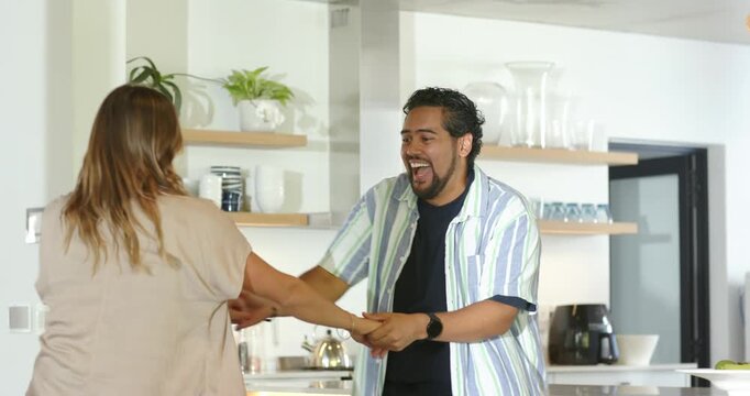 Couple starting playful spin after man entering smiling reaching hands, dancing near kitchen island