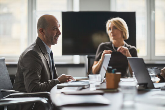Adult businessman leading meeting in office, discussing strategy with colleague using laptops. Ideal for corporate communication, teamwork, leadership campaigns