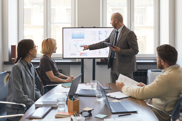 Businessman presenting analytics dashboard to colleagues during office meeting, pointing at screen and discussing strategy. Useful for business reporting, teamwork, planning © DragonImages