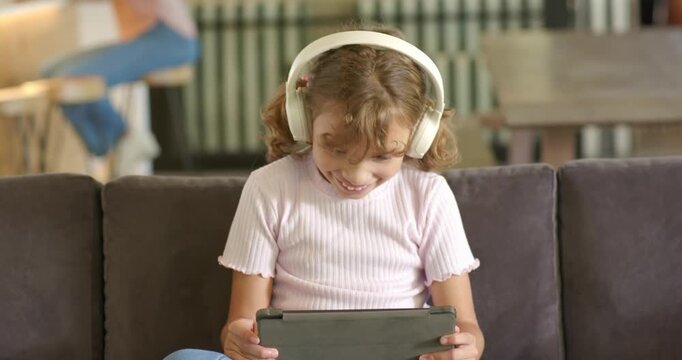 African American child watching tablet for fun at home on couch wearing white headset and smiling