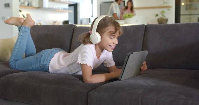 African American girl watching tablet and tapping screen, smiling on sofa at home wearing headset
