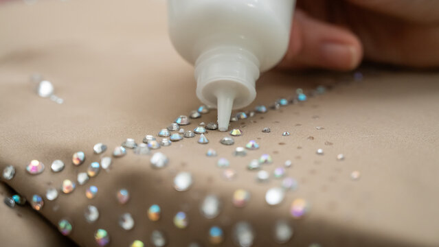 A woman decorates a gymnastics costume with rhinestones. Rhythmic gymnastics. Glue in a tube.