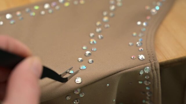 A woman glues rhinestones onto a gymnastics costume using a soldering iron. Hot fix.
