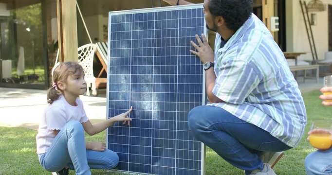 Family patio lawn holding solar panel, child pointing cells, man showing plug, woman holding glass