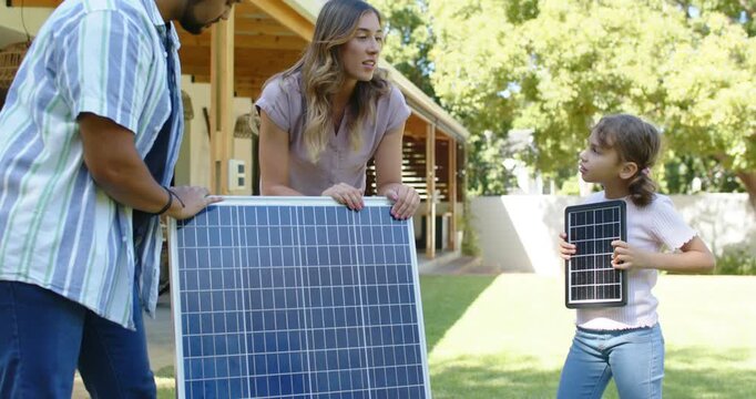 Diverse family holding solar panel in yard, man fixing tangled cable, child holding panel for setup