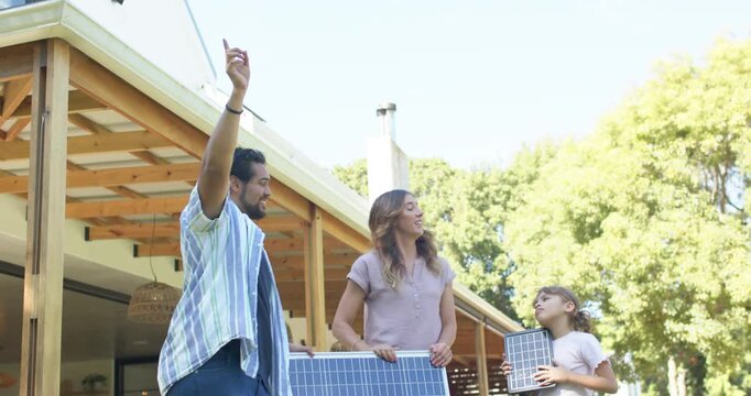 Family man pointing to sun, aiming panel, woman steadying panel, youth girl holding module by patio