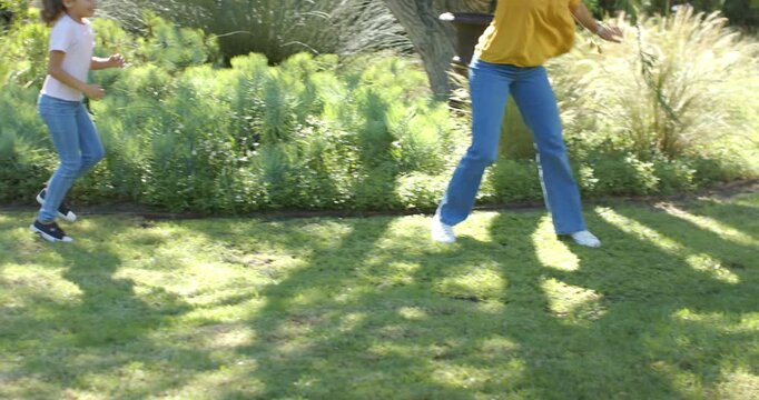 Family entering sunlit yard, woman in yellow blouse playfully chasing child across lawn toward man