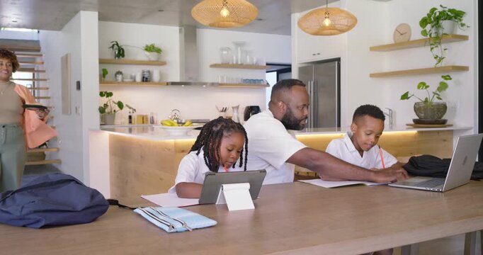 African American family dad guiding daughter on tablet stand while son writing, mom bringing plates