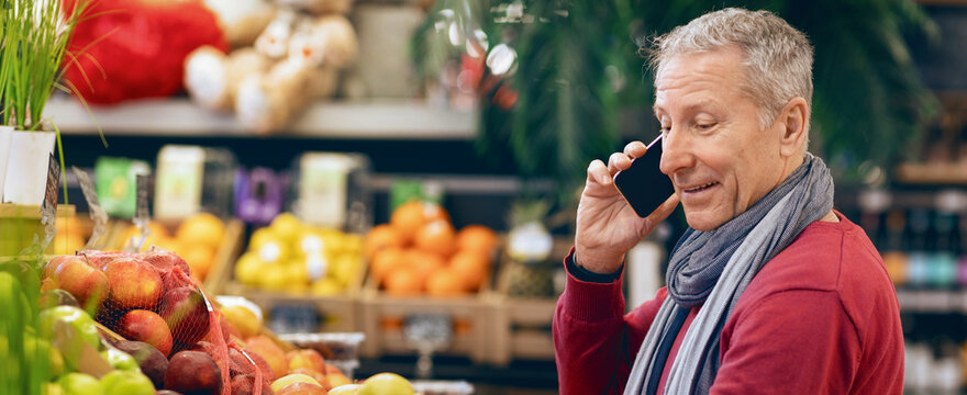 A person is talking on a mobile phone while standing near a display of fruits at a grocery store. The store has many colorful fruits on display.
