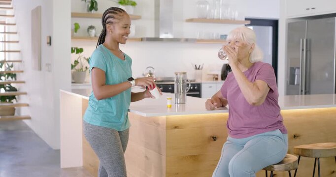 Caregiver handing pill bottle and glass to senior at kitchen island, senior swallowing yellow pill