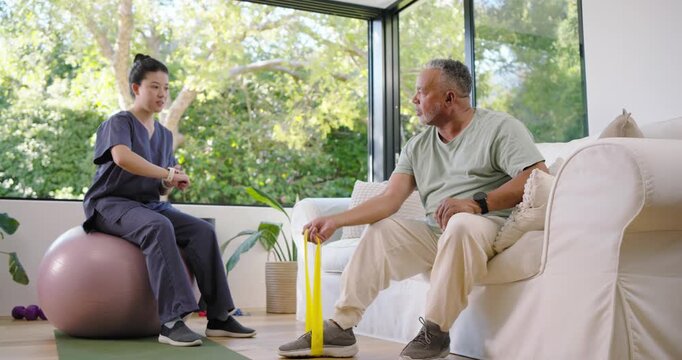 Asian therapist in scrubs timing African American senior pulling yellow band home rehab high-fiving