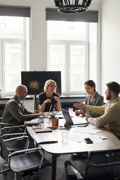 Wide shot of diverse business team discussing strategy during office meeting, collaborating with laptops and documents. Ideal for corporate teamwork, planning, leadership marketing