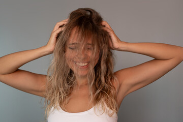 Fototapeta premium Happy smiling young blonde woman touching messy wavy hair with volume and frizz. Playful beauty portrait with porous bleached hairstyle, curly method styling and natural textured hair concept
