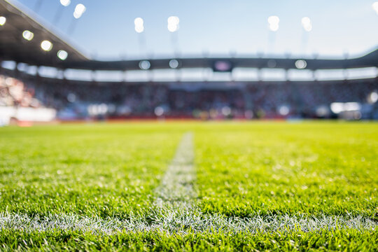 Close-up low-angle view of a white chalk boundary line on a vibrant green soccer pitch with a blurred stadium in the background.
