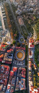 Aerial view of the historic Plaza de toros de La Malagueta bullring surrounded by urban buildings and the green Paseo del Parque boulevard in Malaga, Andalusia, Spain.
