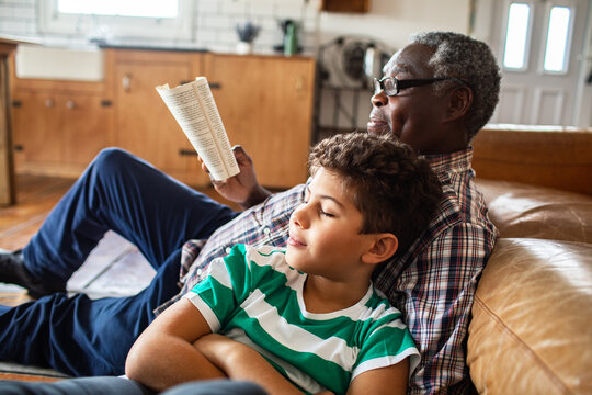Senior man reading with boy on living room sofa