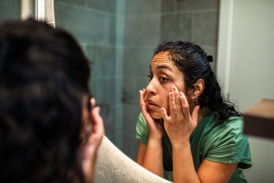 Young woman checking undereye skin in bathroom mirror