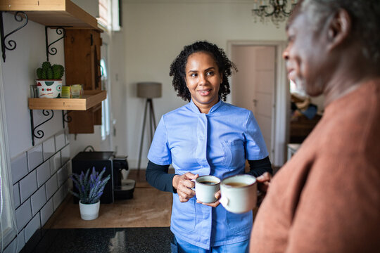 Caregiver offering coffee to senior in home kitchen