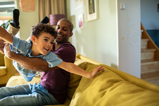 Father lifting son like airplane on sofa at home