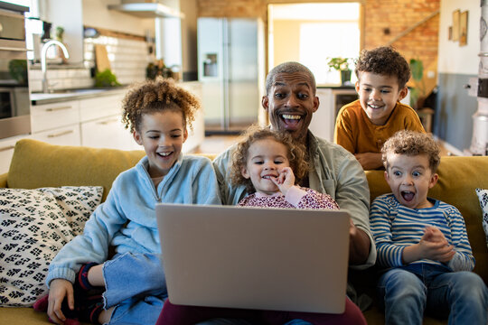 Father with four children watching laptop on sofa at home