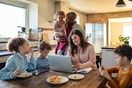 Parents working on laptop with children in home kitchen