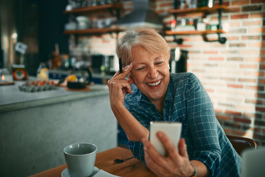 Smiling senior woman using smartphone in home kitchen