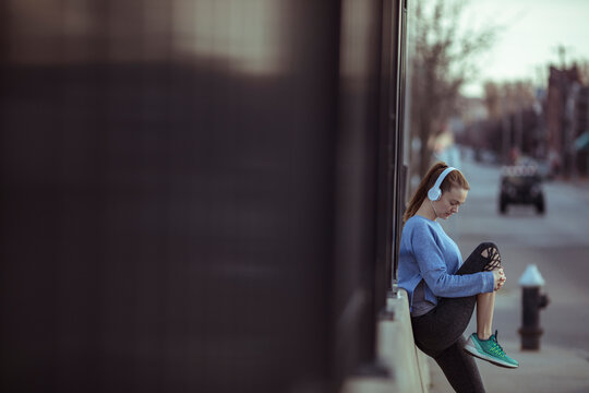 Young woman wearing headphones stretching on city sidewalk