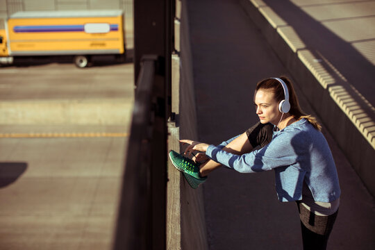 Young woman stretching before run on urban bridge at sunrise