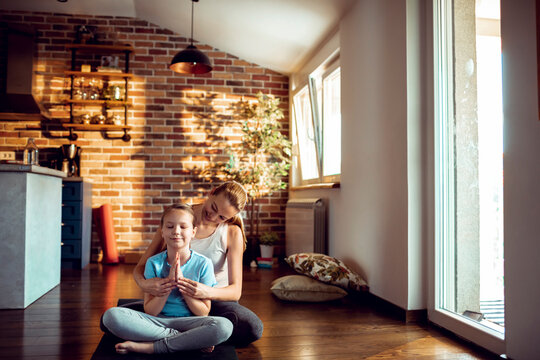Mother guiding daughter in yoga meditation at home