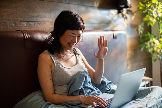 Smiling woman waving on video call in bed at home