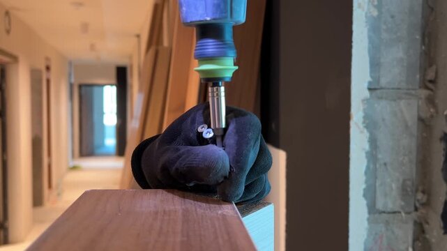 Close up of carpenter hands using electric screwdriver to drill screw into wood.
