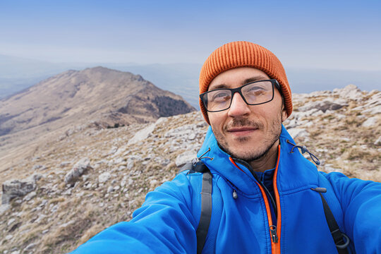 Hiker enjoying personal achievement and freedom at mountain summit, smiling at camera with a rugged landscape